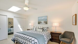 Une chambre à coucher avec un lit, des tables de chevet, une chaise, un ventilateur de plafond et un tableau accroché au mur.