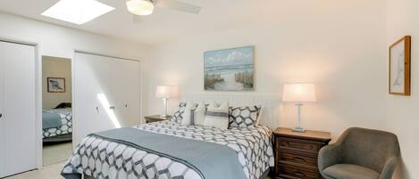 A bedroom with a bed, nightstands, a chair, a ceiling fan, and a painting on the wall.