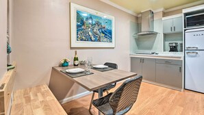 A dining area with a wooden table, wicker chairs, a framed cityscape painting, and a kitchen with a white refrigerator and cabinets. - Romantic Pasadena Home w/ Covered Porch! (Pasadena)