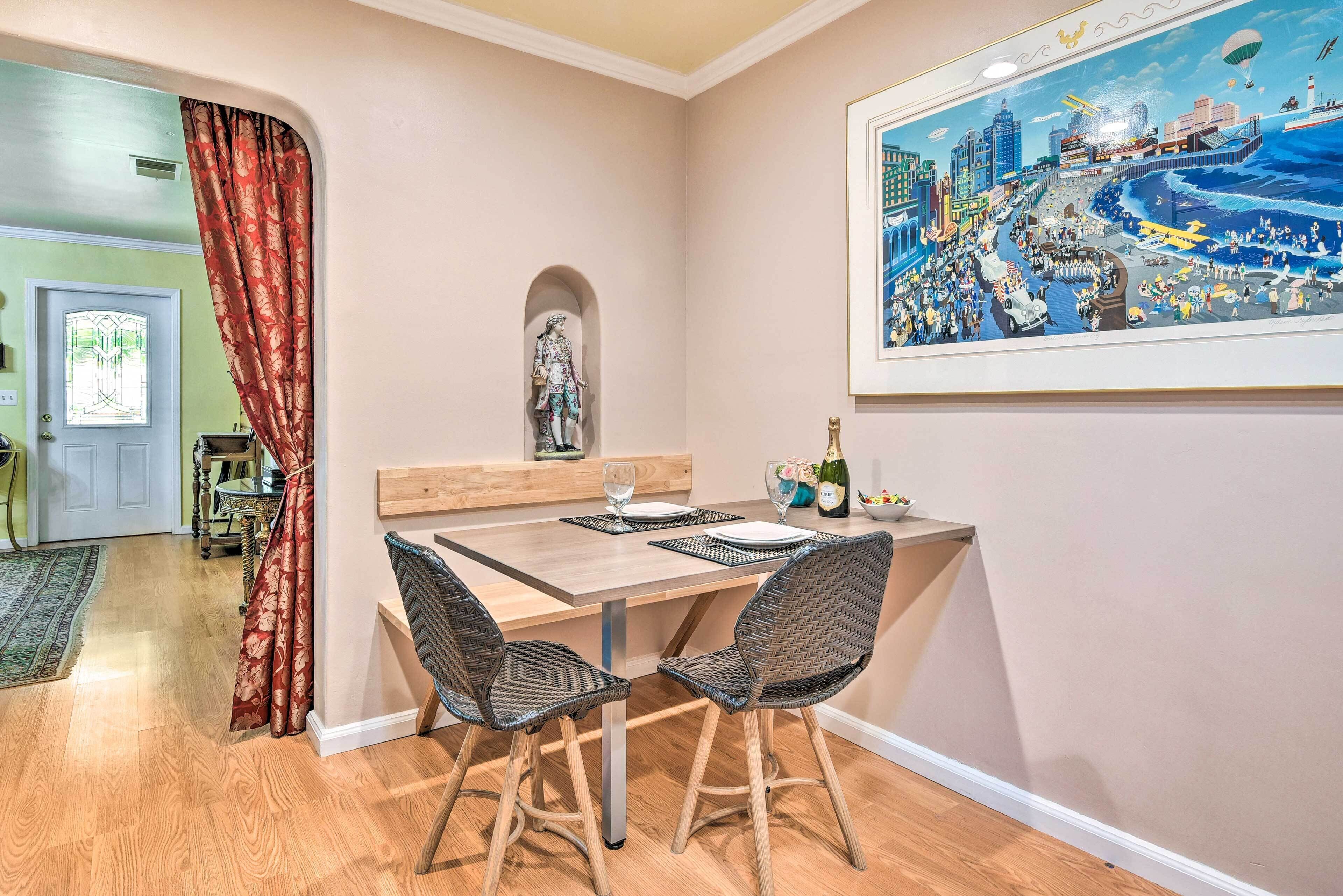 Un área de comedor con una mesa dispuesta para dos personas, una estatua y un cuadro de gran formato con una vista urbana.
