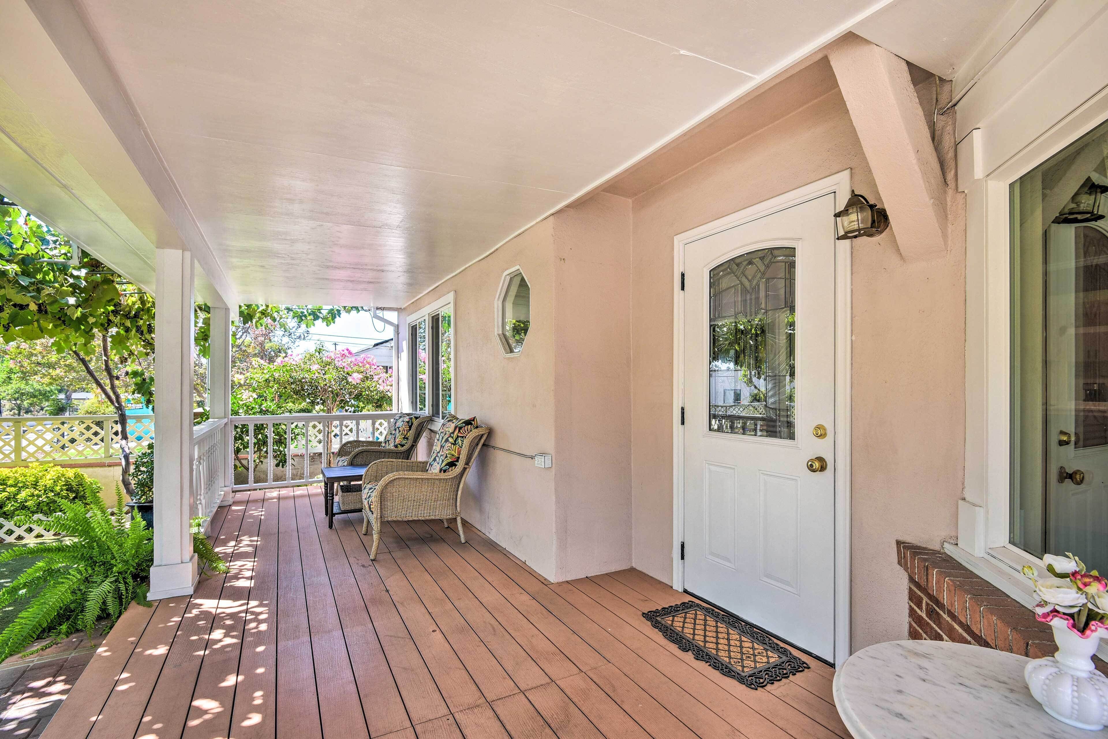 A covered porch with a white door, wicker furniture, and a small table with a vase.