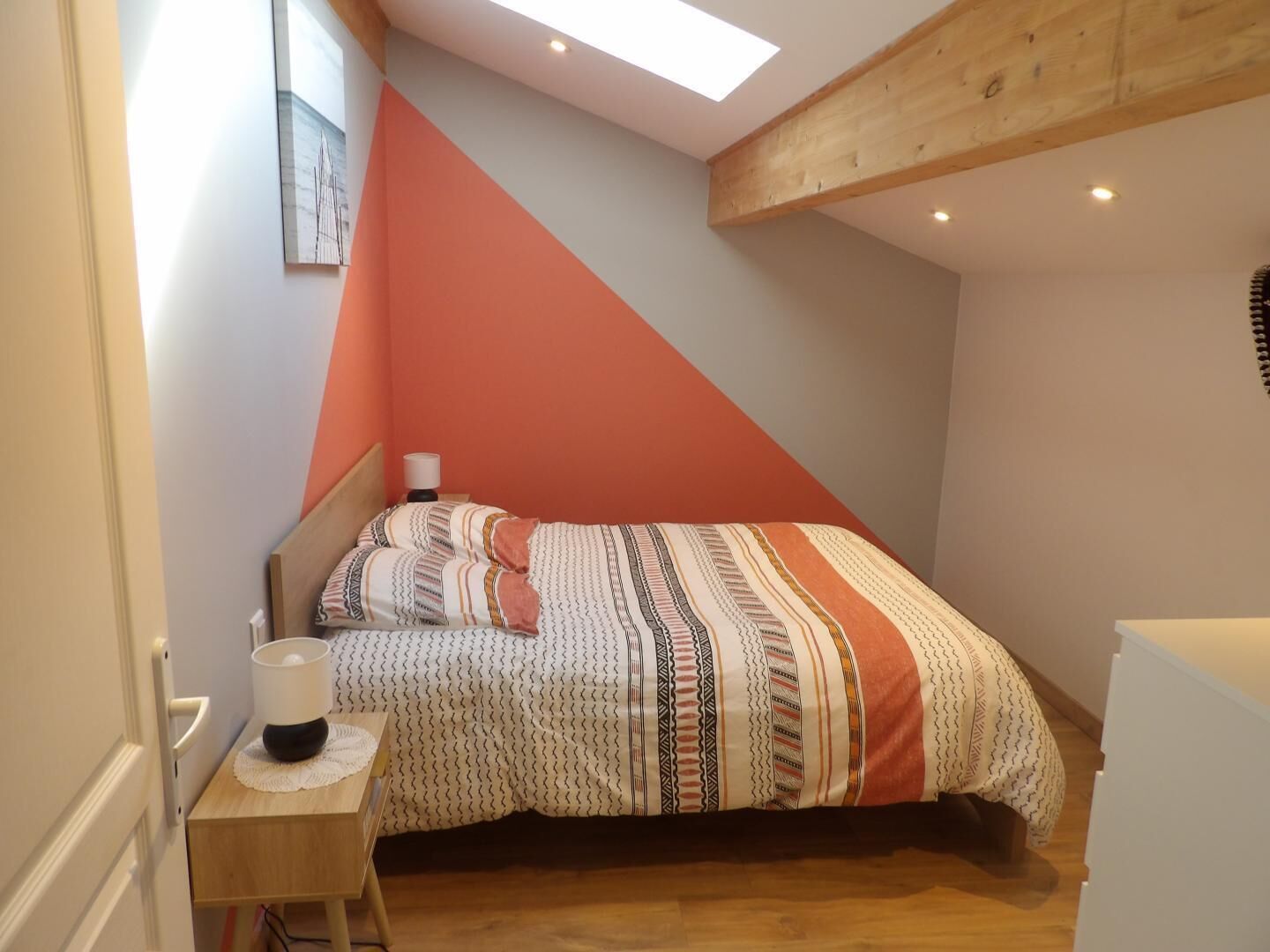 A bedroom with a sloped ceiling, a bed with patterned bedding, a bedside table with a lamp, and a small desk.