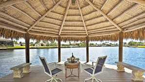 A covered outdoor seating area with a thatched roof, overlooking a body of water. - Luxe Cape Coral Escape w/ Boat Dock + Cabana! (Cape Coral)