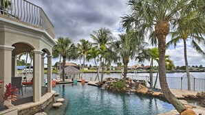 A pool area with palm trees, a water feature, and a view of a body of water. - Luxe Cape Coral Escape w/ Boat Dock + Cabana! (Cape Coral)