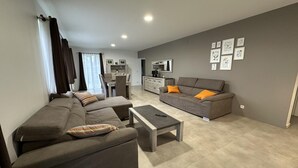 Un salon moderne avec un canapé, une table basse et un téléviseur. On aperçoit à l’arrière-plan un coin repas avec une table et des chaises.