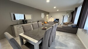 Un salon moderne comprenant un coin repas, des canapés gris, une table basse et un téléviseur.