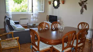 Un comedor con una mesa de madera redonda, seis sillas de madera, un televisor y un jarrón decorativo.