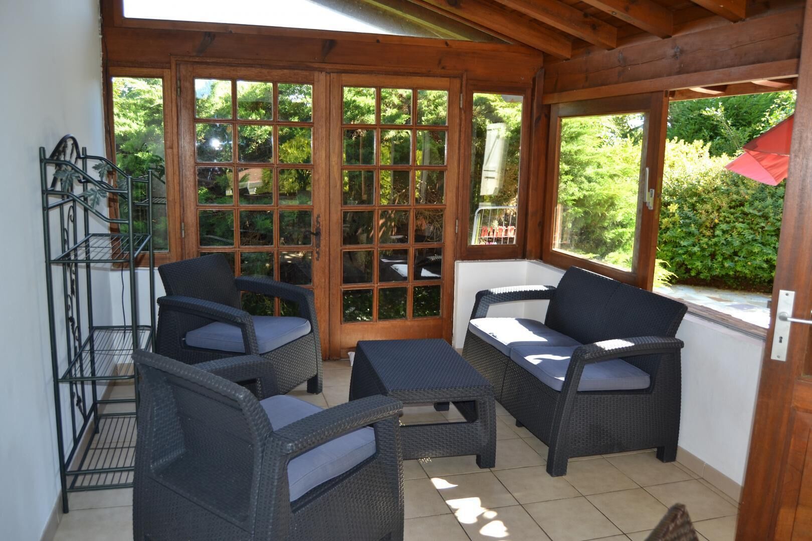 A covered patio area with wicker furniture, a metal rack, and a view of greenery outside.