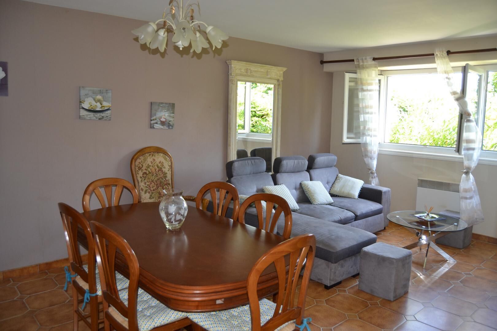 A dining area with a wooden table and chairs, a grey sofa, and a small side table with a lamp.