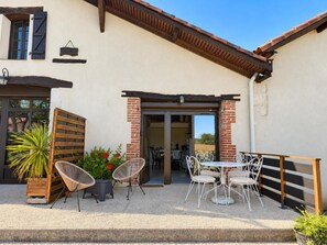 Un patio con mobiliario exterior, un muro de ladrillo y una puerta que da a un espacio interior.