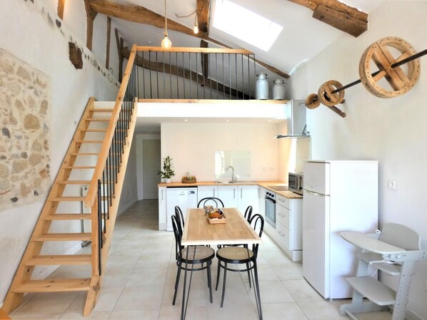 Una cocina moderna con una escalera de madera, un comedor con mesa y sillas, y un refrigerador blanco.