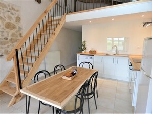 Una cocina moderna con armarios blancos, una mesa de comedor de madera y una escalera con barandilla de madera.