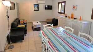 A compact living space with a sofa, a small table, a dining table with chairs, a TV, and a cabinet. - Lou Parc - Leon - Gîte (LEON)