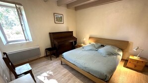 A bedroom with a bed, a wooden dresser, a desk, a radiator, and a window. - Escapeteu - AZUR - Gîte (AZUR)