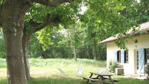 A rustic house with a large tree in the foreground, a picnic table, and two lawn chairs. - Escapeteu - AZUR - Gîte (AZUR)
