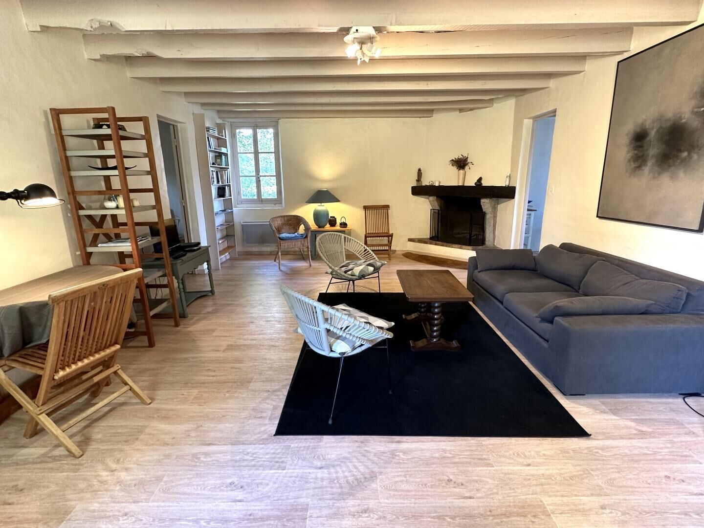 A spacious living room with a grey sofa, a wooden coffee table, and a black rug. There is a fireplace, a bookshelf, and a ladder against the wall.
