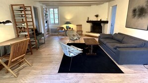 A spacious living room with a grey sofa, a wooden coffee table, and a black rug. There is a fireplace, a bookshelf, and a ladder against the wall. - Escapeteu - AZUR - Gîte (AZUR)