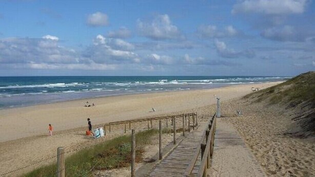 A beach with a wooden boardwalk leading to the water, sandy beach, and ocean waves. - Escapeteu - AZUR - Gîte (AZUR)
