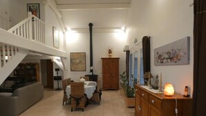 Ein geräumiges Wohnzimmer mit hoher Decke, einem Essbereich mit Korbstühlen, einer Treppe und einem Kamin.