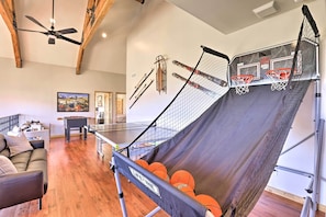 A room with a ping pong table, a sofa, and a wall with skis and basketball hoops.