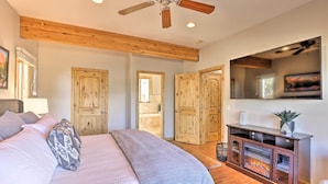 Ein Schlafzimmer mit einem großen Bett, Holzbalkendecke, Kamin und einem an der Wand befestigten Fernseher.
