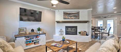 Una sala de estar con chimenea, ventilador de techo, televisor montado y mesa de centro con revistas.