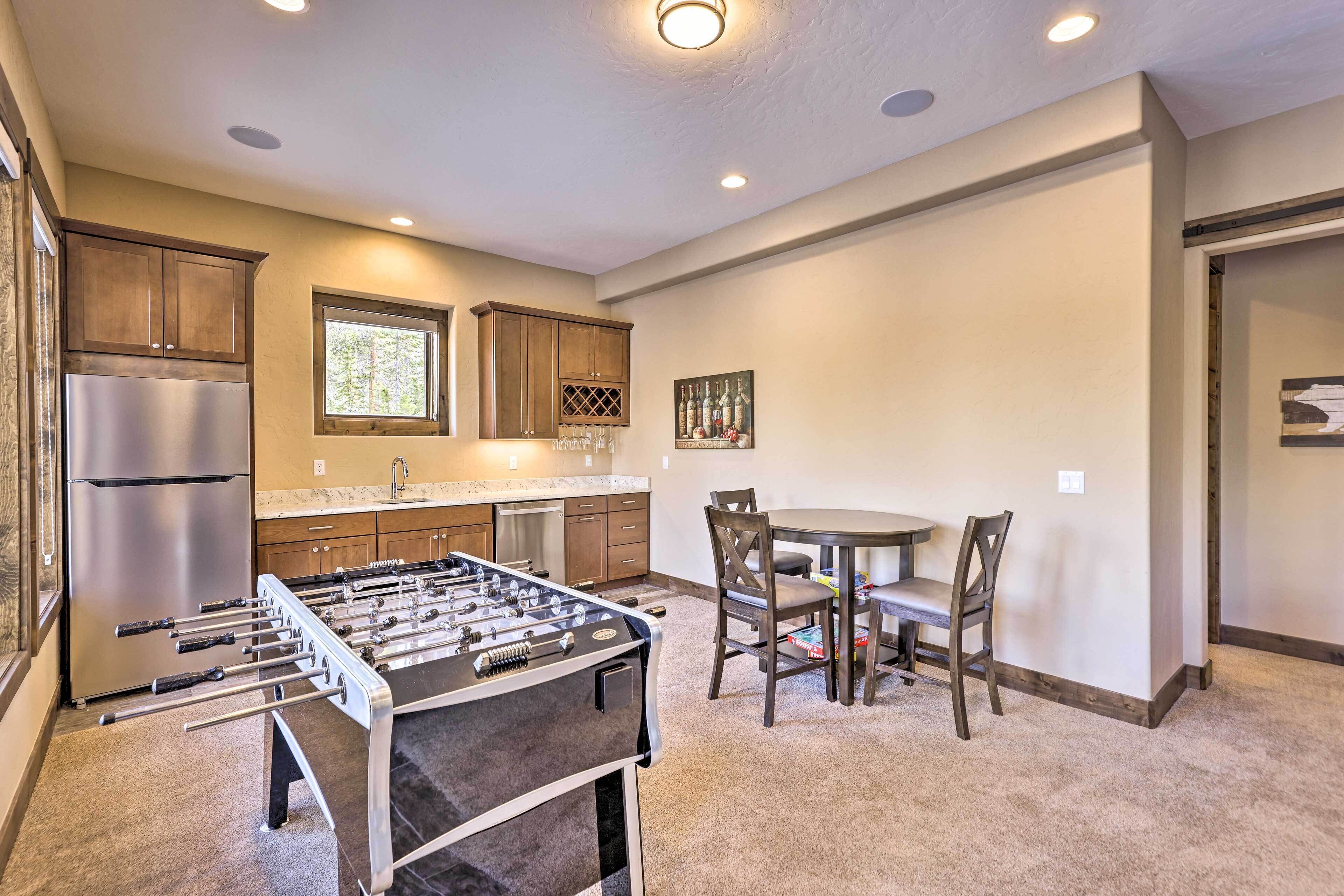 A kitchen with a foosball table, a refrigerator, and wooden cabinets.