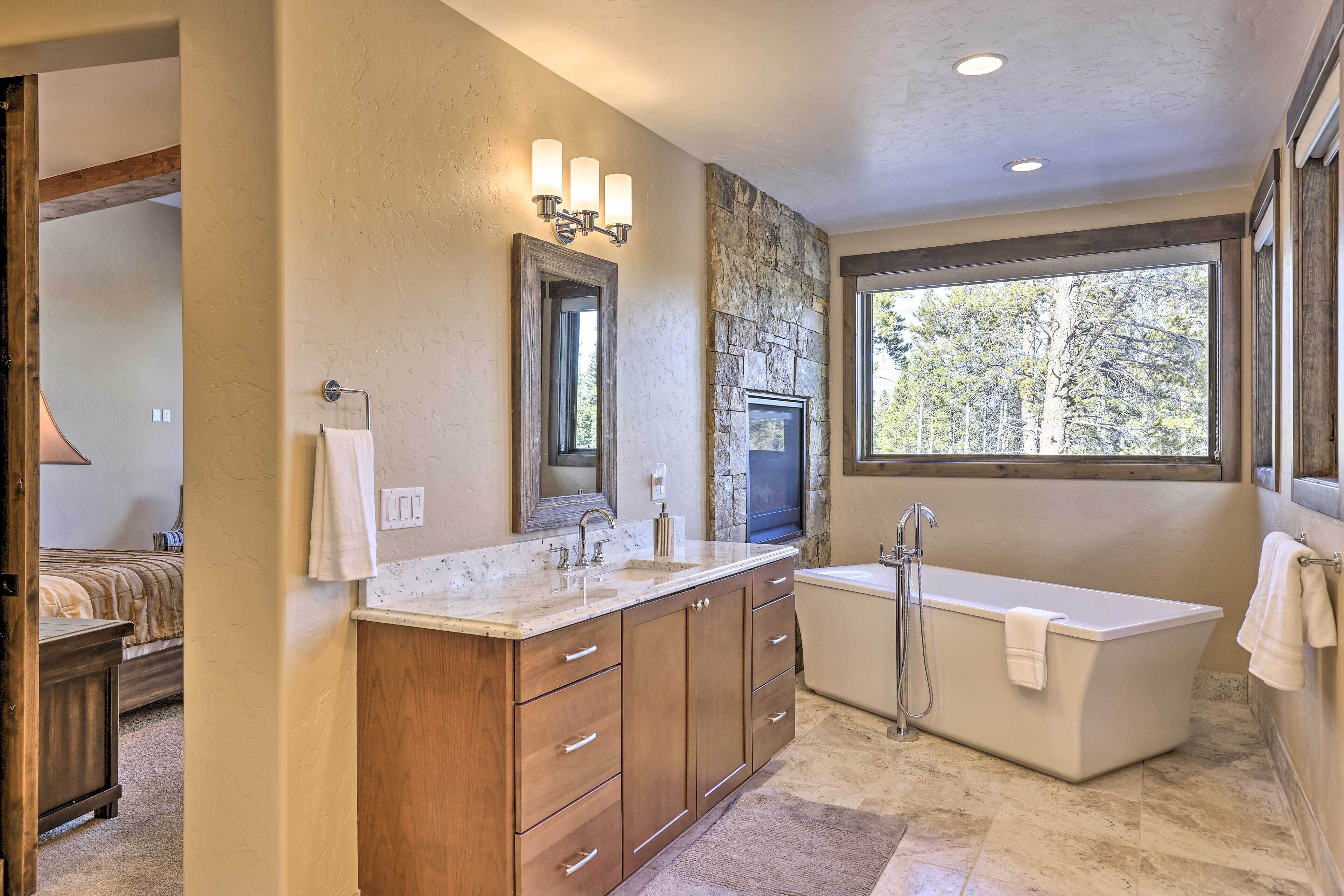 A modern bathroom with a freestanding bathtub, a large mirror, and a stone accent wall.