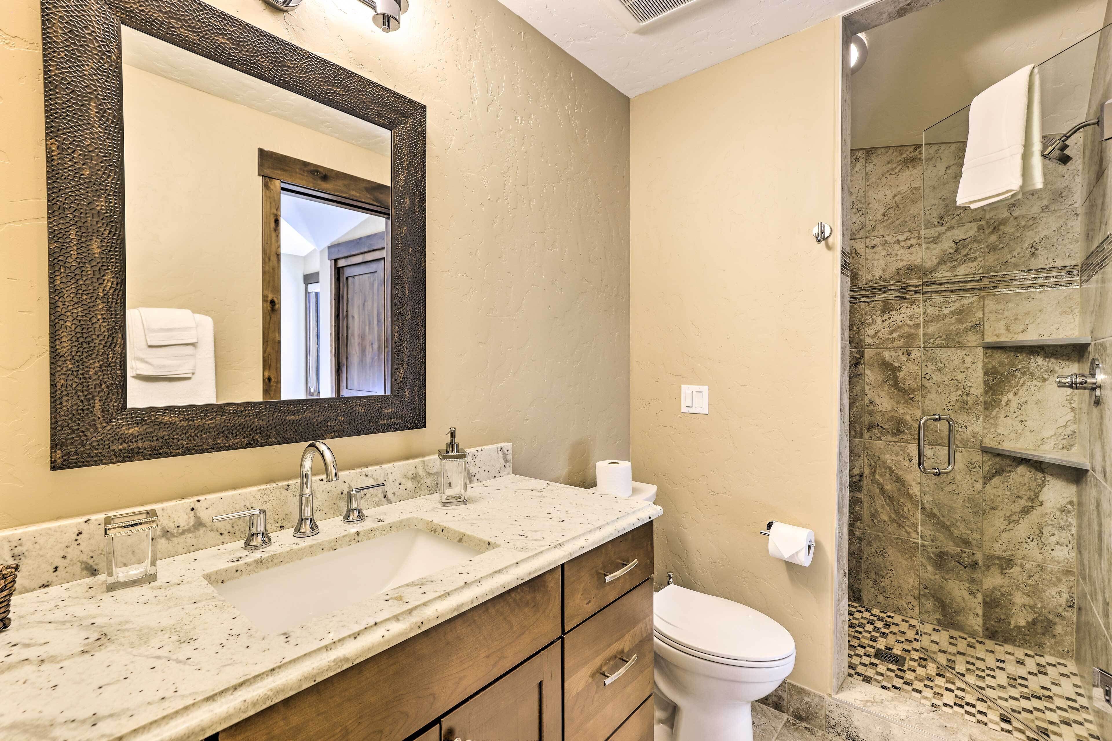 Une salle de bain avec un lavabo en marbre, un grand miroir, des toilettes et un espace douche doté d’un carrelage à motifs géométriques.