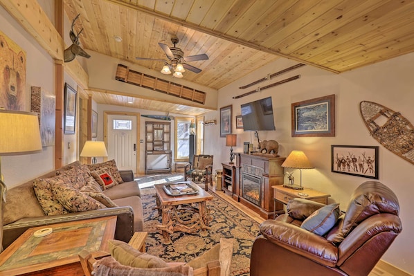 A cozy living room with a fireplace, leather sofa, and a ceiling fan.