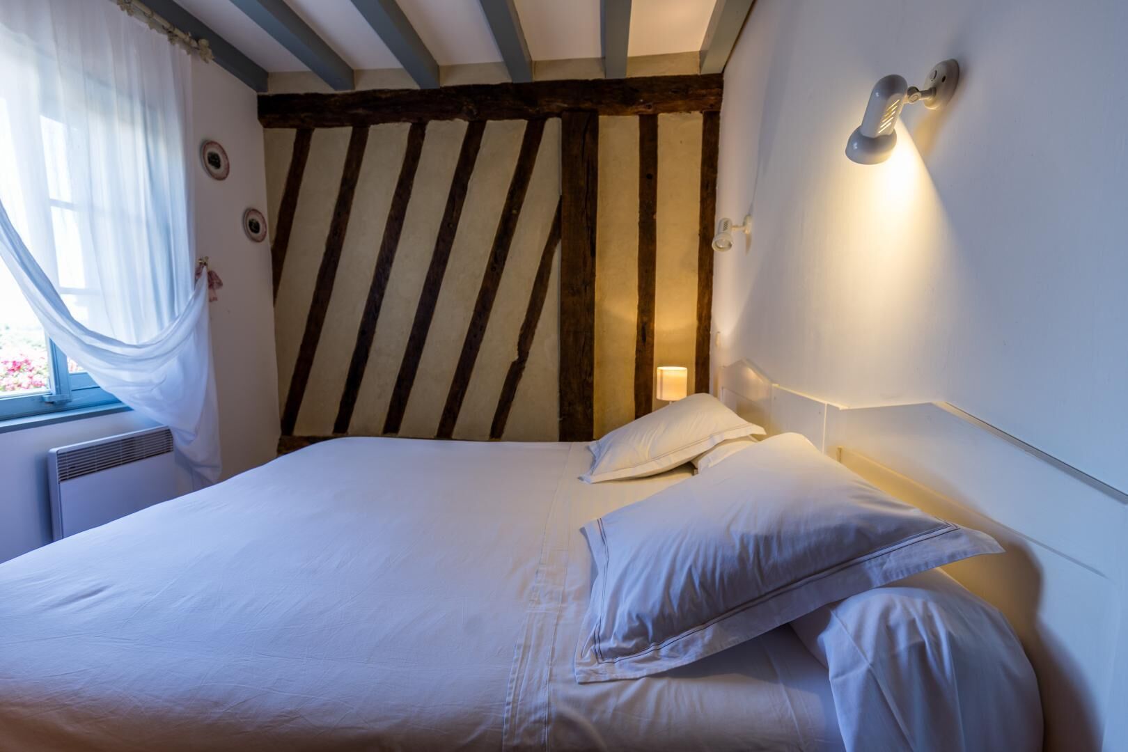A bedroom with a slatted headboard, a bed with white linens, and a wall-mounted light fixture.