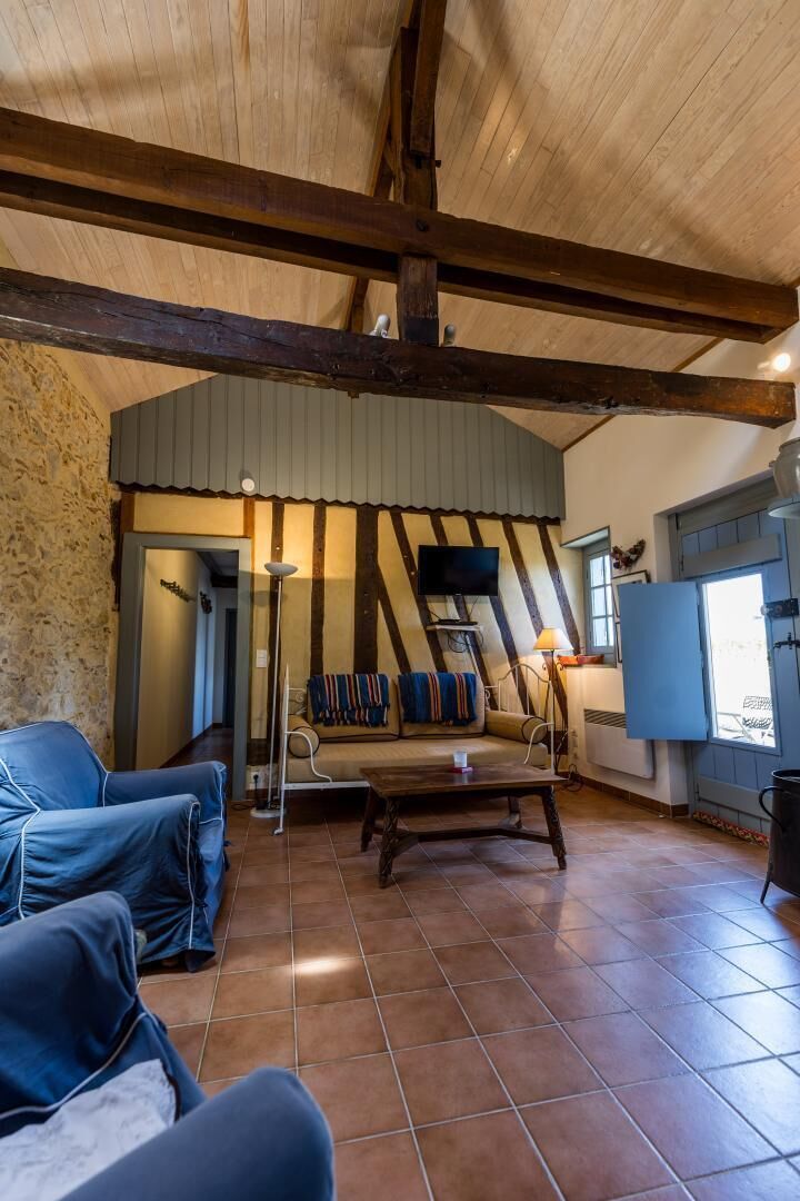 Un intérieur rustique avec des poutres apparentes, un sol carrelé, un ensemble de canapés, un téléviseur et une fenêtre offrant une vue agréable.
