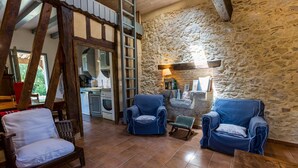 A rustic interior with stone walls, wooden beams, and a kitchen in the background.