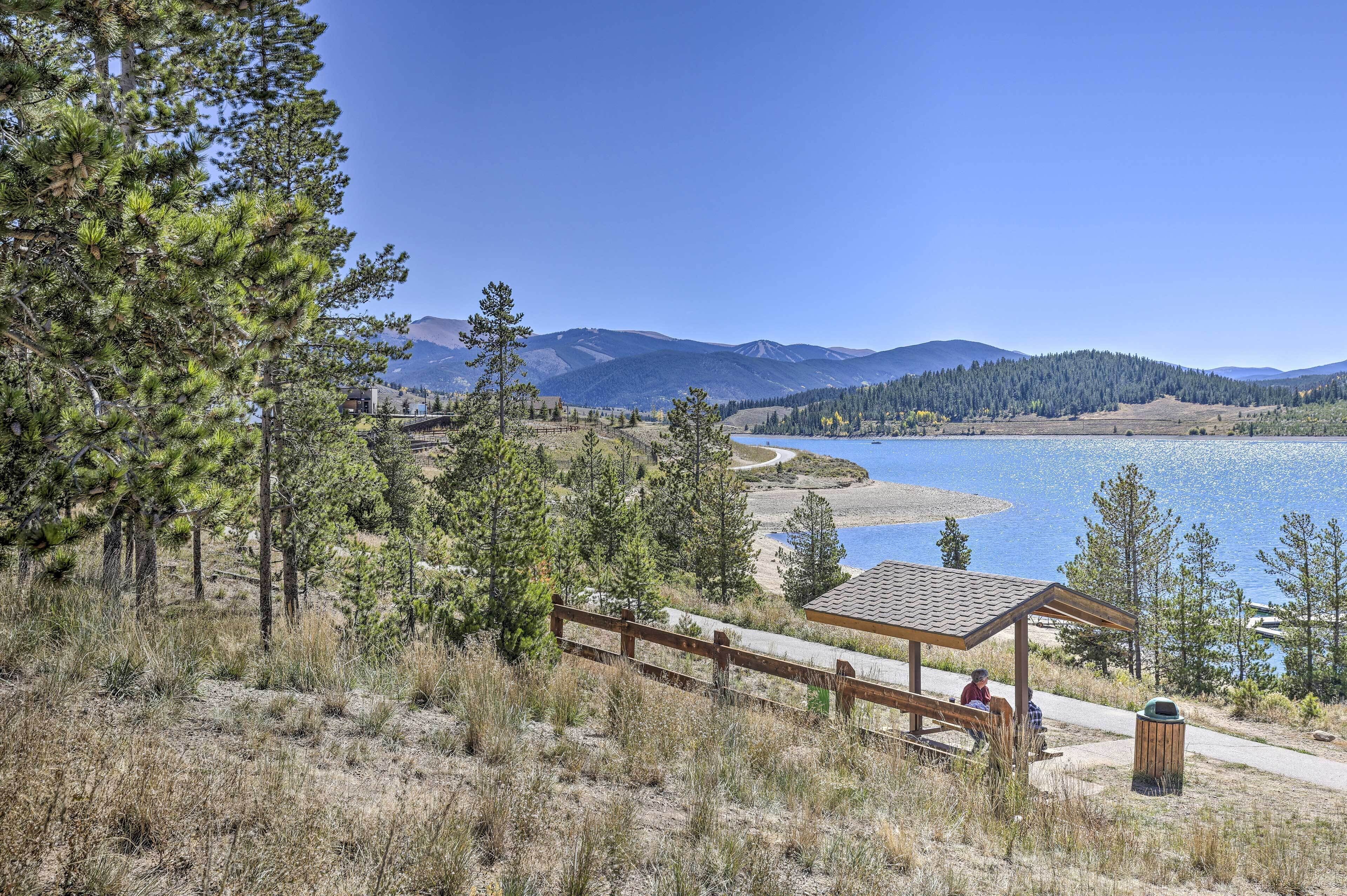 A lakeside view with a wooden pavilion, picnic tables, and a clear sky.