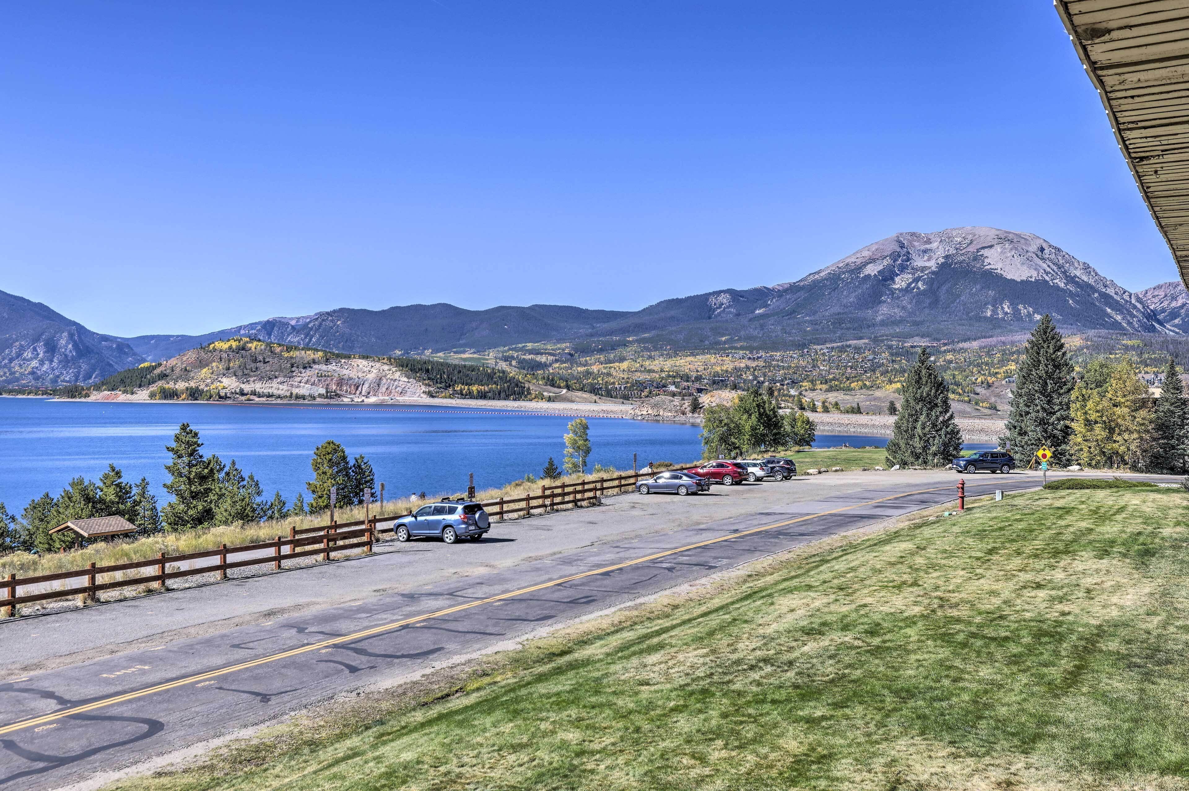Un estacionamiento con coches, una valla de madera y vistas a un lago y montañas.
