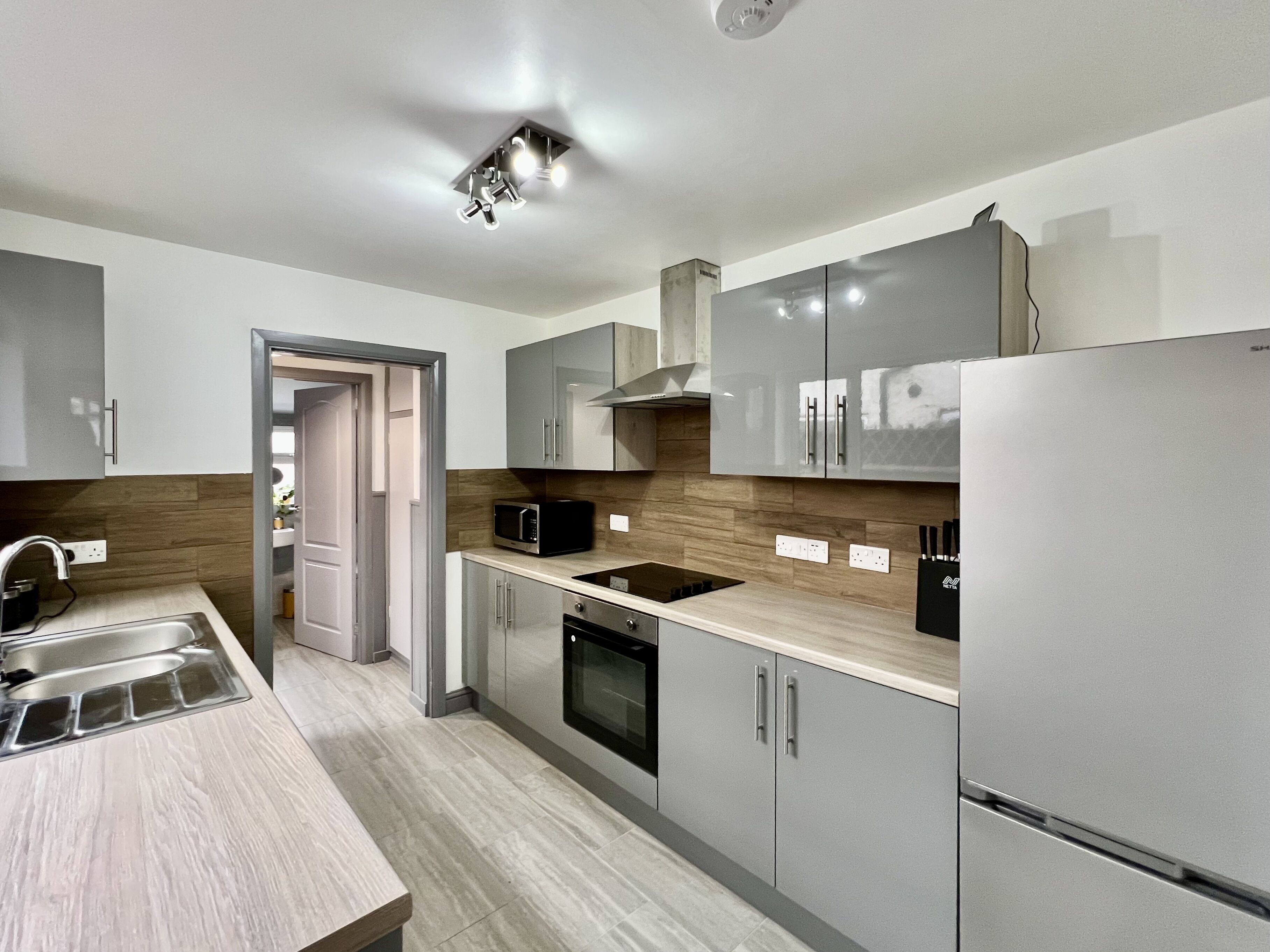 A modern kitchen with grey cabinets, a stainless steel refrigerator, a microwave, and a built-in oven.