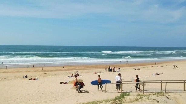 A beach with people walking and sitting, and a person carrying a surfboard. - L'ecureuil - Soustons (SOUSTONS)