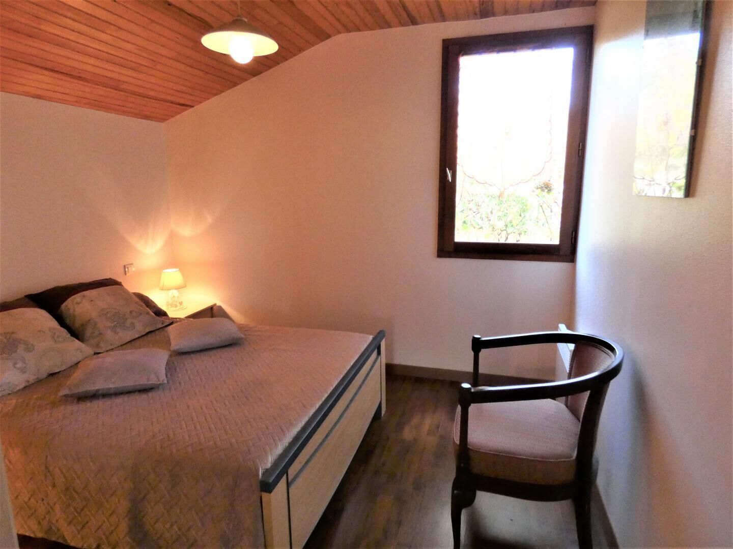 Une chambre à coucher avec un lit, une chaise, une fenêtre et une lampe.