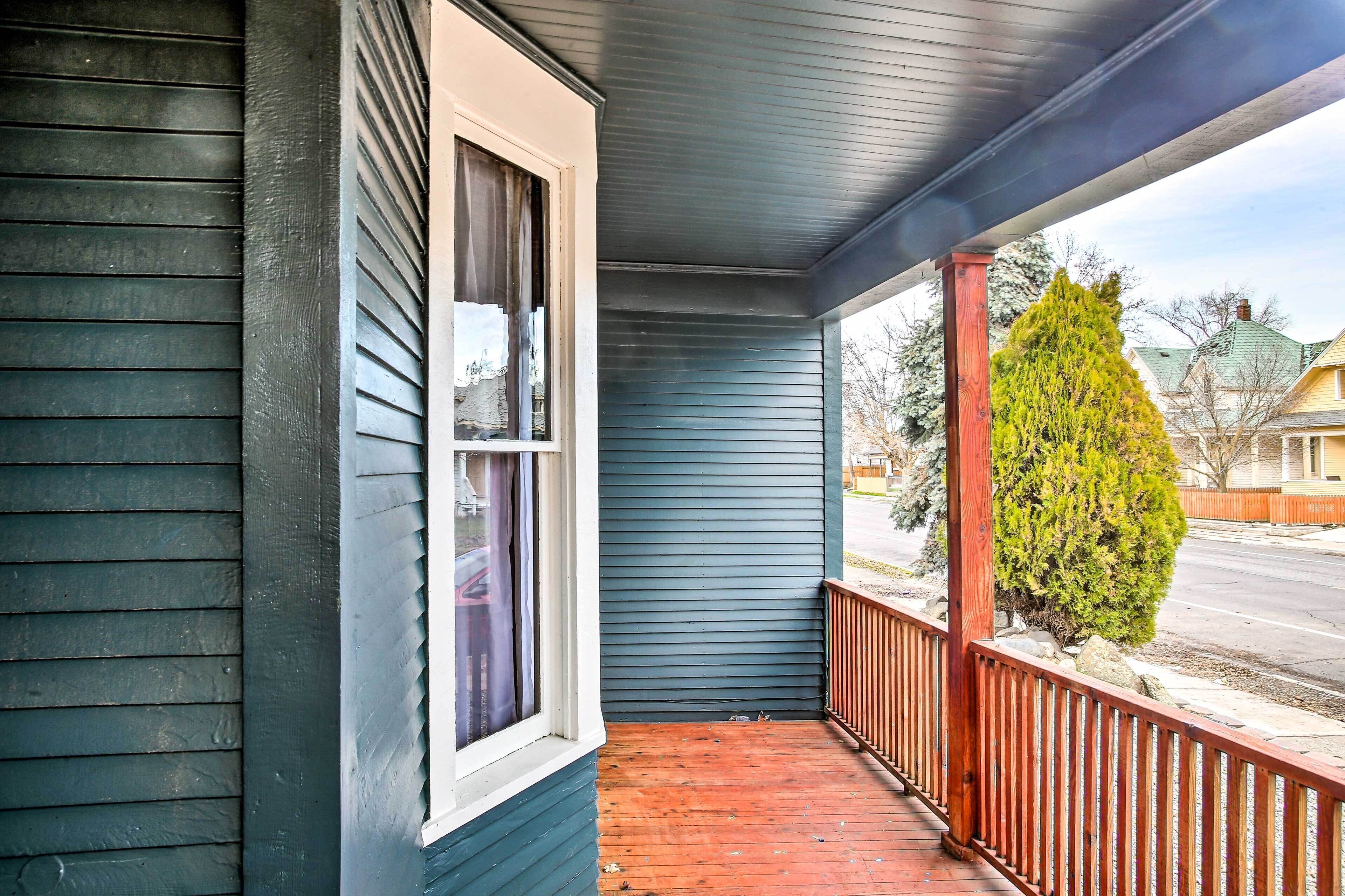 A porch with a wooden railing, a window with a white frame, and a green tree in the background.