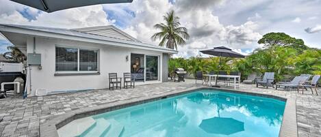Una piscina con zona de patio, mobiliario exterior y una casa con garaje.
