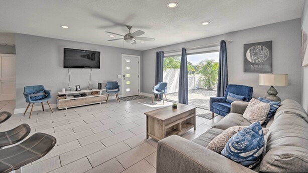 A modern living room with a flat-screen TV, ceiling fan, and a large window with curtains. - Remodeled Naples Getaway w/ Pool ~ 1 Mi to Beach! (Naples)