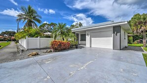 A single-story house with a garage, surrounded by a white fence, palm trees, and a concrete driveway. - Remodeled Naples Getaway w/ Pool ~ 1 Mi to Beach! (Naples)