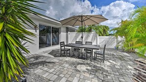 An outdoor patio with a table and chairs, a large umbrella, and a white building with a glass door. - Remodeled Naples Getaway w/ Pool ~ 1 Mi to Beach! (Naples)