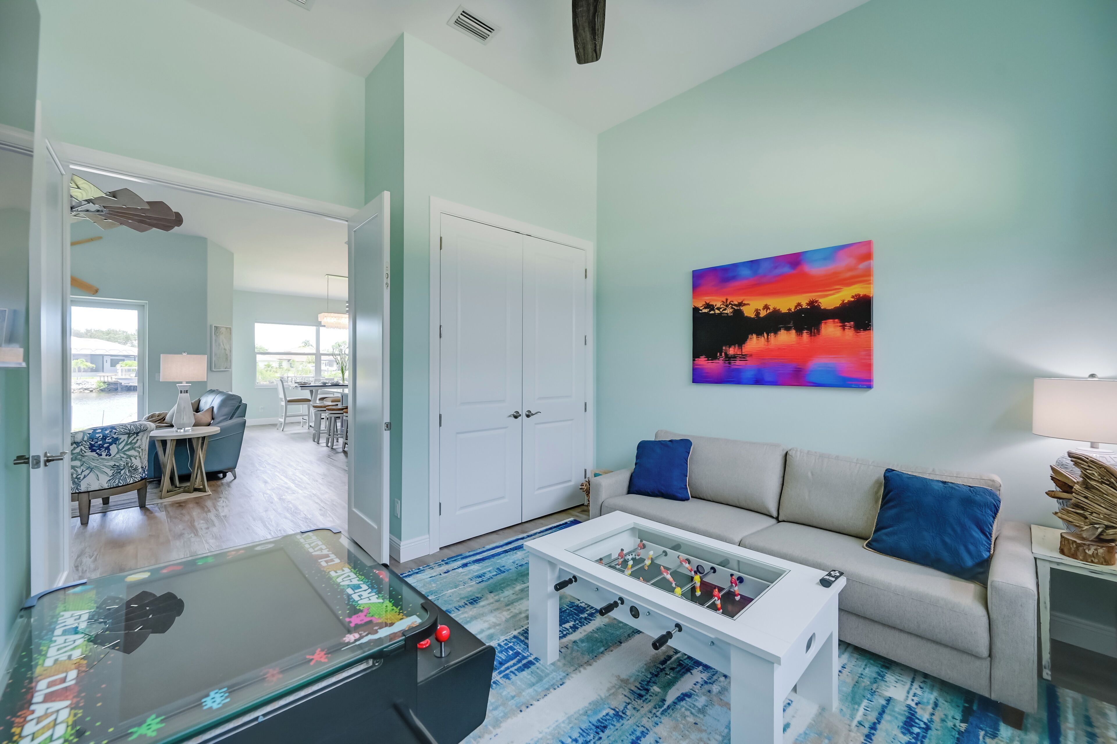 A living room with a foosball table, a sofa, a coffee table, and a painting on the wall.