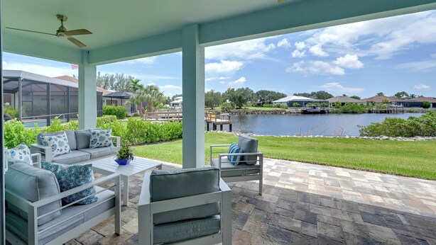 A covered patio with outdoor furniture, a view of a lake, and a boat dock. - Luxurious Canal-front Retreat w/ Game Room! (Naples)