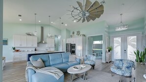 A spacious living area with a blue sofa, a round coffee table, and a ceiling fan. - Luxurious Canal-front Retreat w/ Game Room! (Naples)