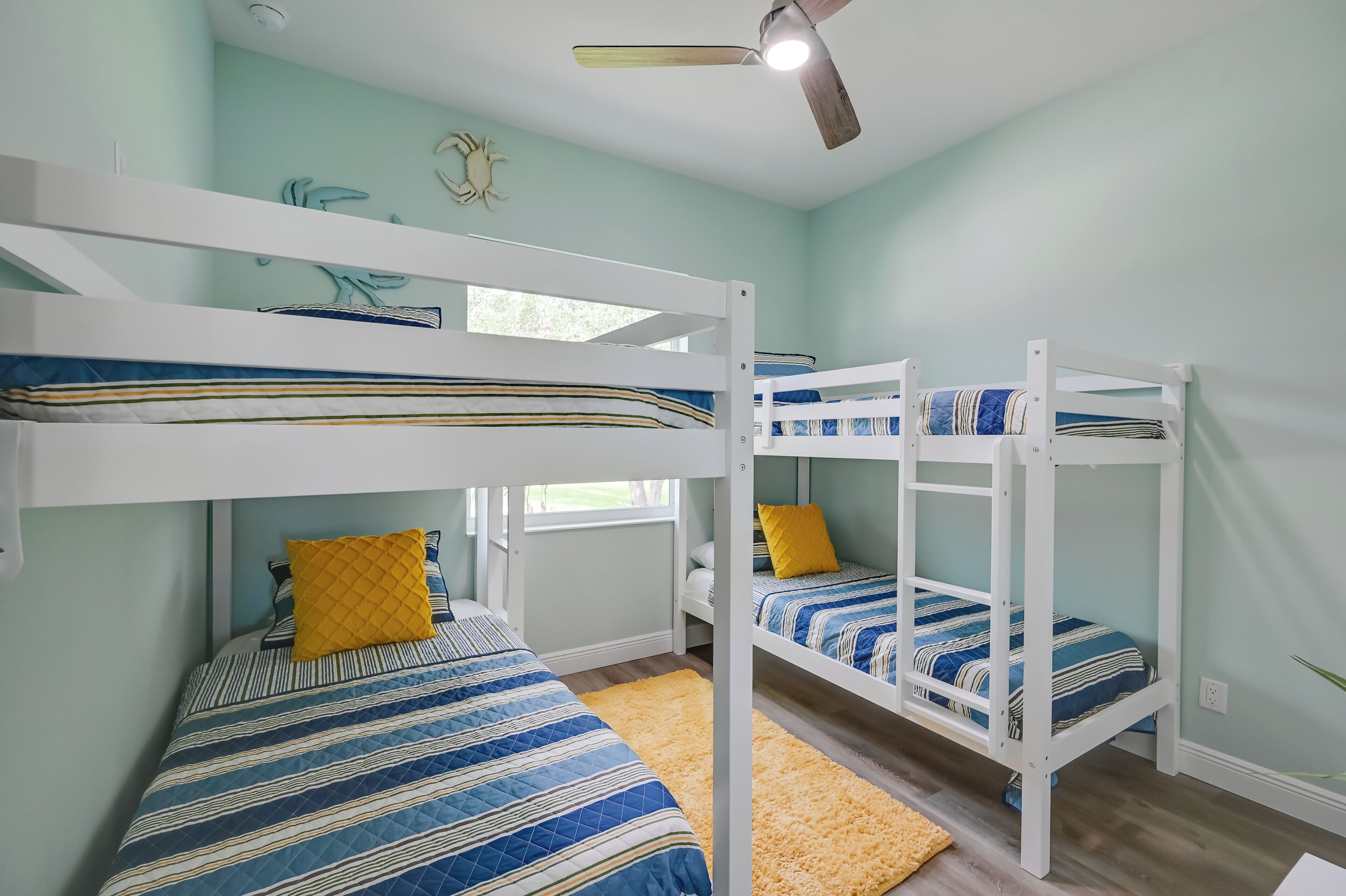 Habitación con literas, ventilador de techo, ventana y una alfombra amarilla.