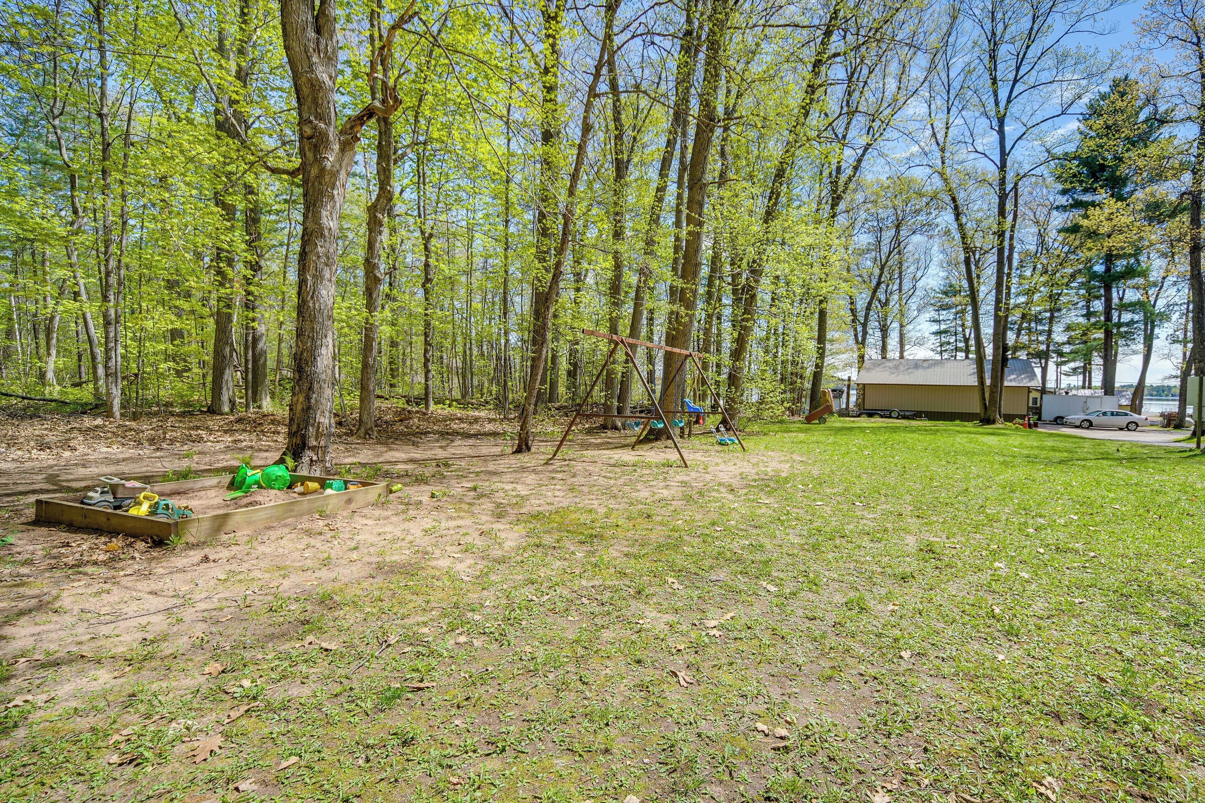A wooded area with a swing set, a small shed, and a grassy field.