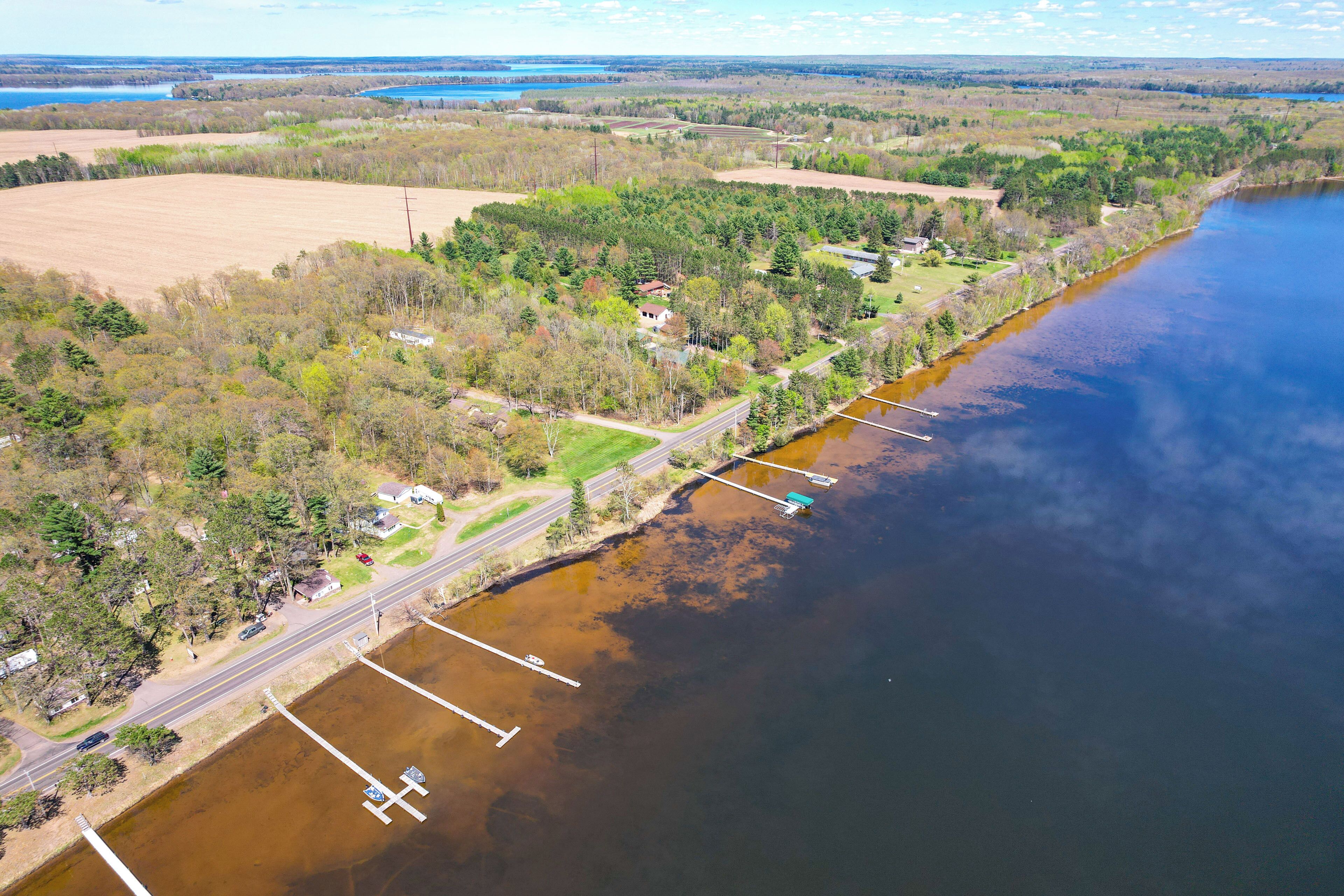 Vue aérienne d’une propriété au bord d’un lac, avec une route, un quai et une végétation luxuriante tout autour.