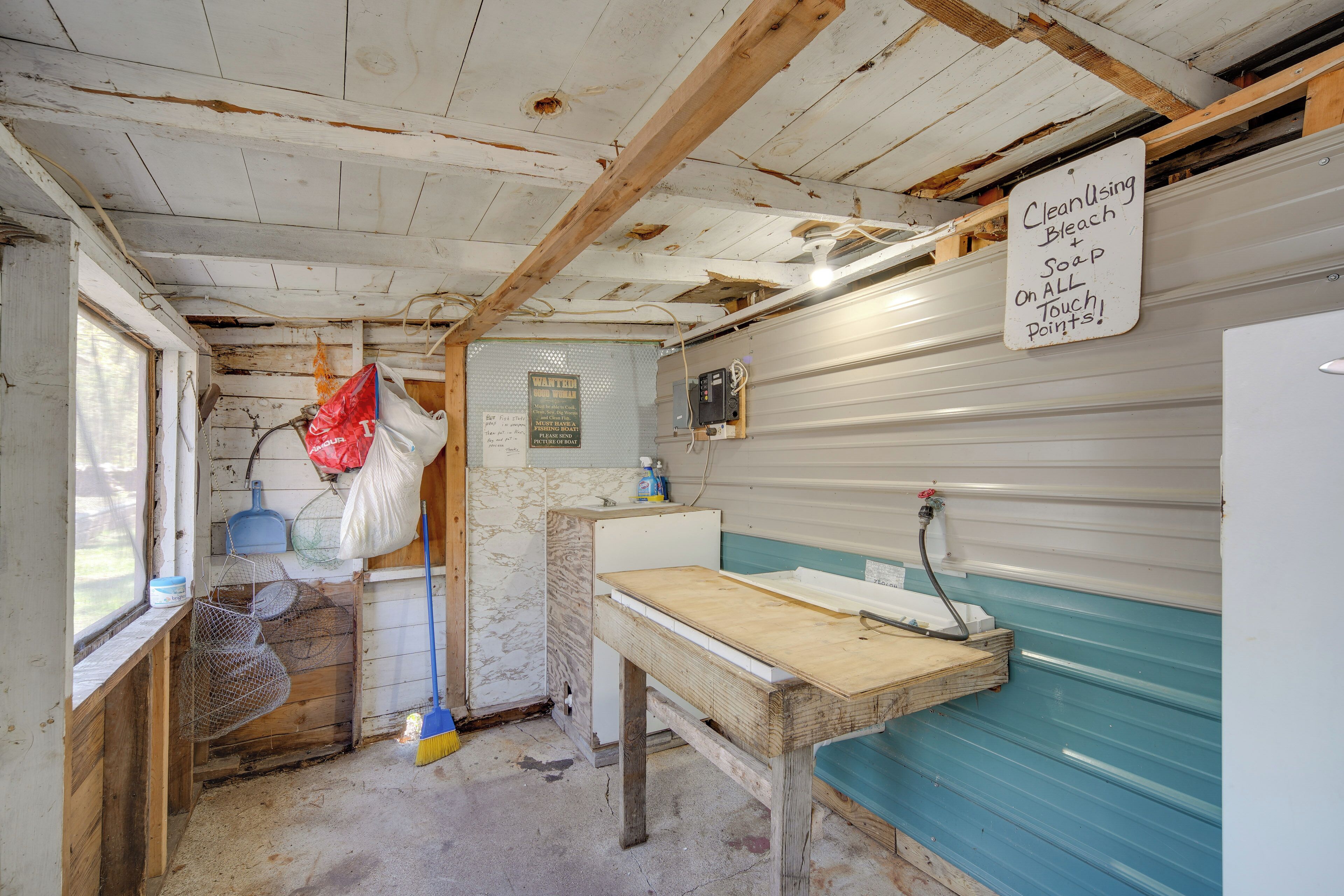 A small, rustic bathroom with a wooden bench, a sink, and a sign instructing to use bleach and soap on all touch points.